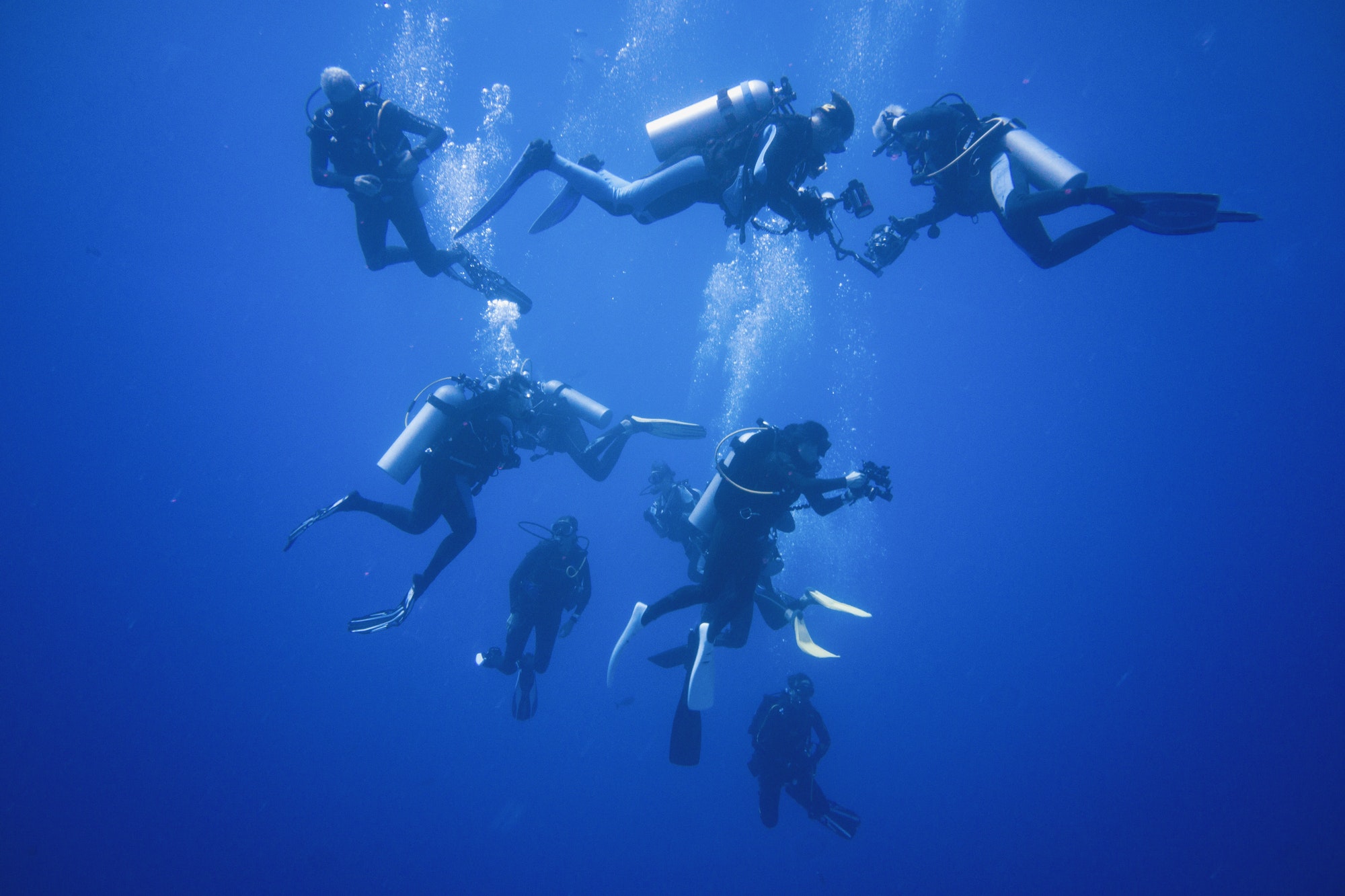A group of scuba divers descending into infinite blue waters.
